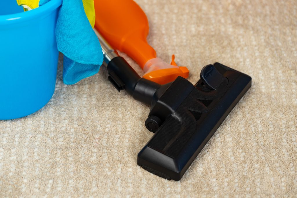 Red vacuum cleaner and plastic bucket with liquid detergents on beige carpet
